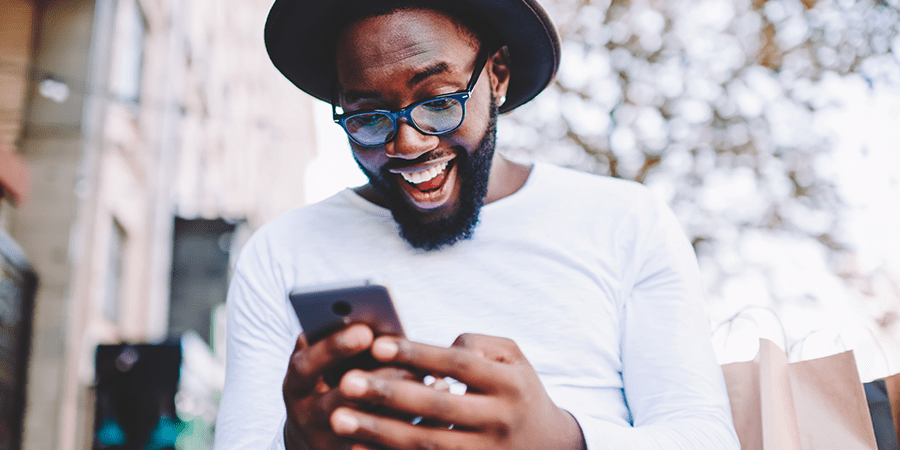 A young man looking at his smartphone with a big smile.