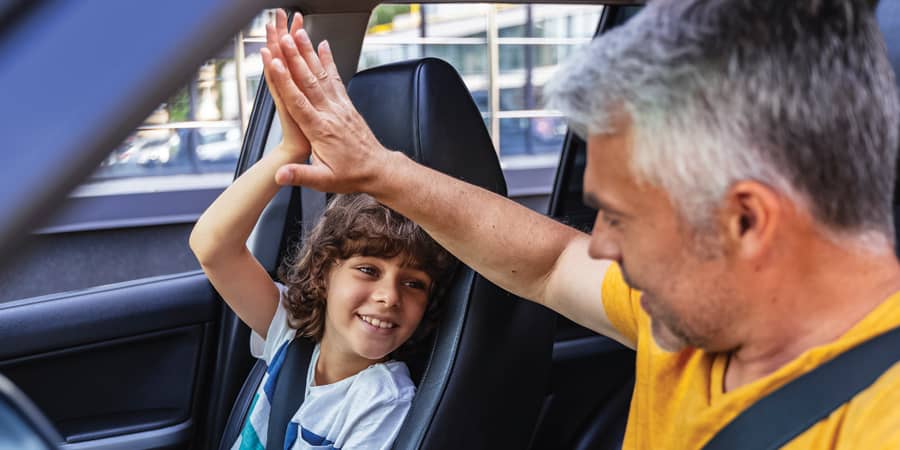 A father high fives his son inside of a new car.