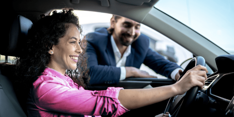A car salesman leaning into the driver's side window with a woman sitting in the driver's seat.