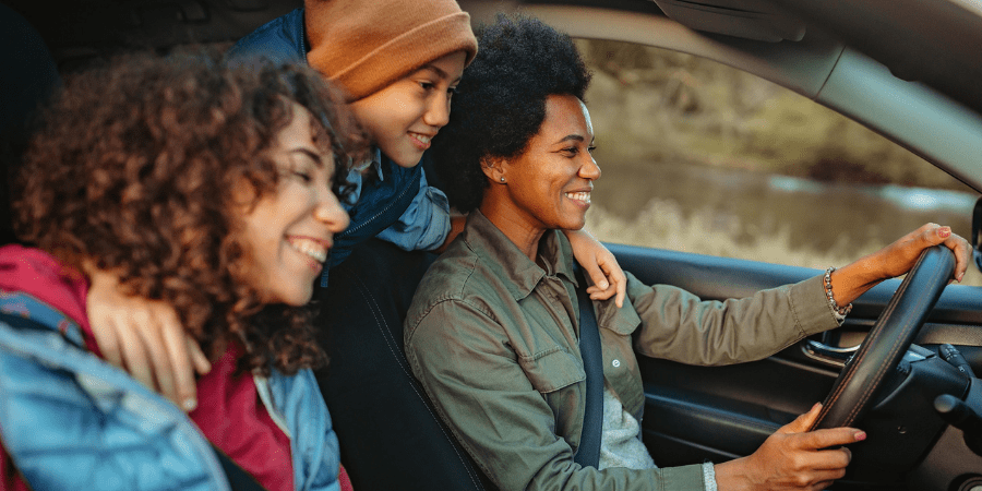 Two women in a car and a young child looking from the back seat.