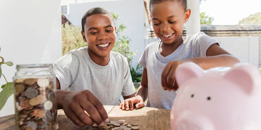 Two siblings happily collecting pennies into a glass jar.