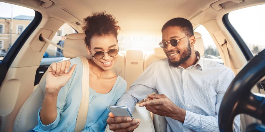 A young, fashionable couple inside a new car looking at a mobile phone.
