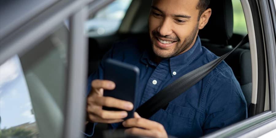 A young man sitting in a car looking at a smart phone.