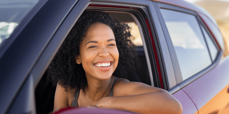 A woman smiling while sitting in the driver's seat of a car.
