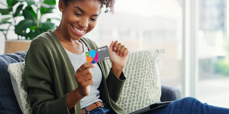 A young woman sitting on a couch holding the EdFed Rewards Visa Credit Card.