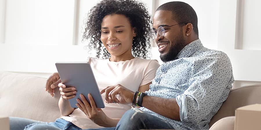 A young couple sitting together on a couch sharing a tablet.