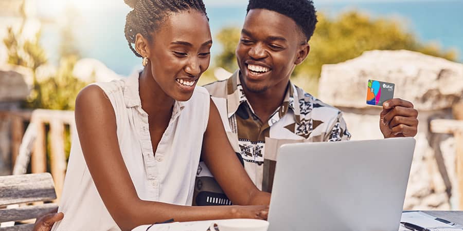 A young couple sitting at a table using a laptop while holding the EdFed credit card.