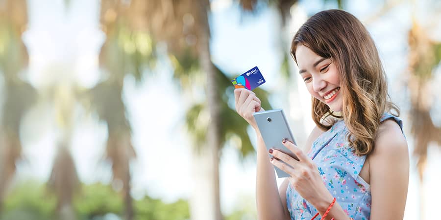 A young woman happily holding the EdFed Rewards card and looking at her mobile phone.