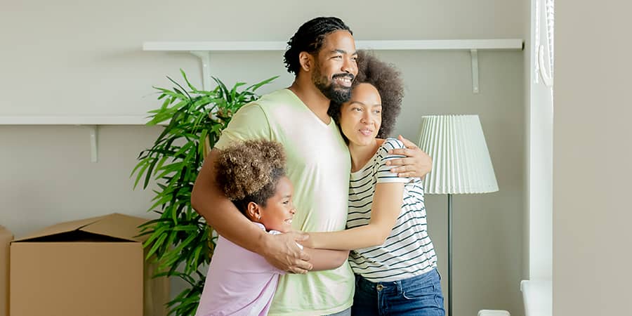 A young family embracing each other in a living room containing move boxes.