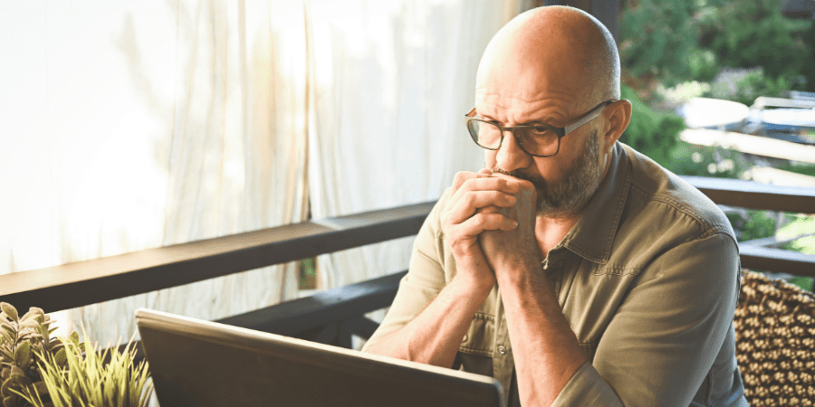 An older man looking at a laptop with a concerned expression.