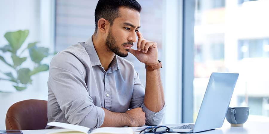 A young man sitting at a desk intensely looking at a laptop.