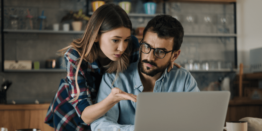 A woman pointing to a laptop used by a man sitting at a table.