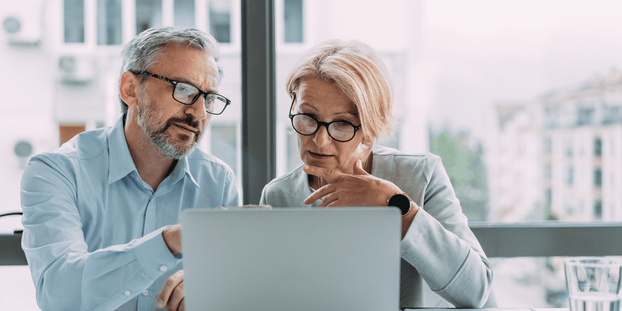 An elderly couple sitting together looking at a latpop.