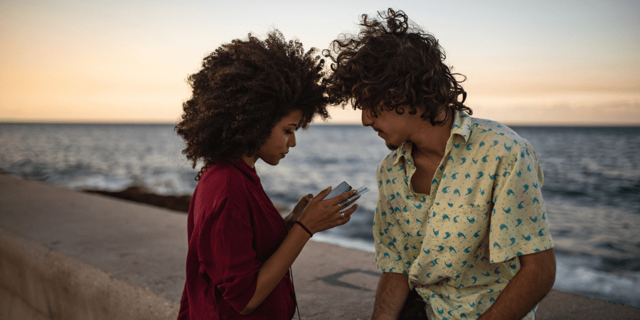 A young couple sitting on a ledge overlooking a beach while holding credit cards.