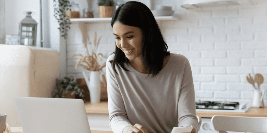 A young woman sitting at a kitchen counter looking at a laptop.