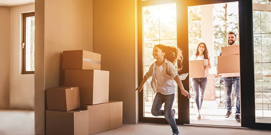 A family of three entering their home carrying moving boxes.