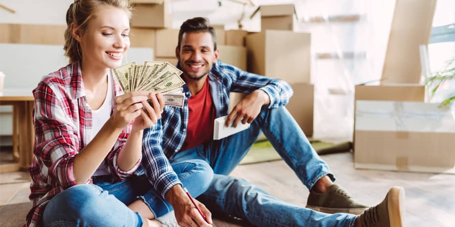 A young couple sitting on the floor of their newly moved in home counting $100 dollar bills.