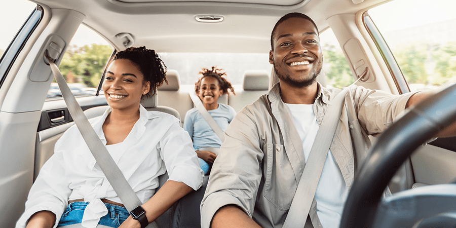 A young family of three driving in a car while smiling.
