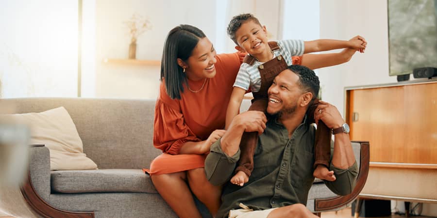 A young family of three sitting in their living room smiling at each other.