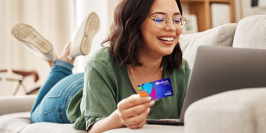A young woman laying on a couch holding the EdFed Visa Credit Card.