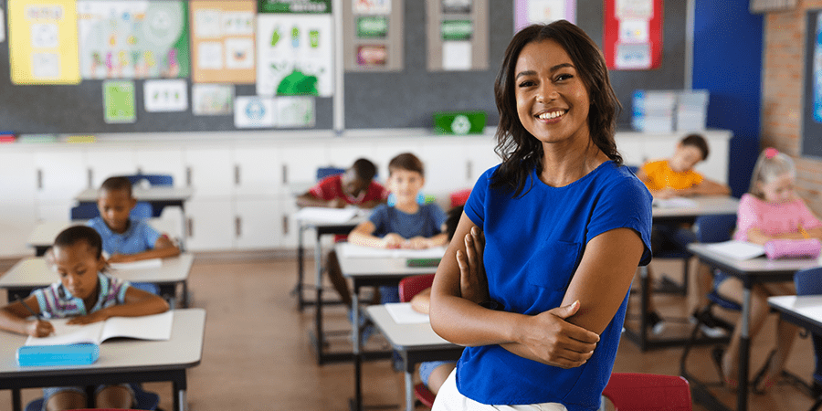 A young woman teacher standing in the middle of a classroom smiling.