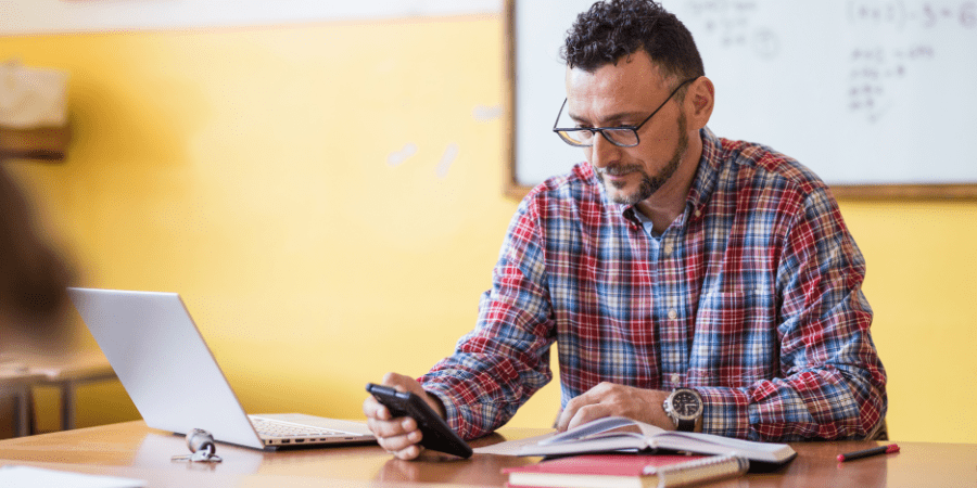 A man holding and looking at a mobile phone at his desk.