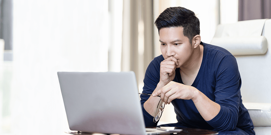 A young man sitting on a couch intensely looking at a laptop.