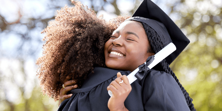 Two femail graduates embracing eachother.