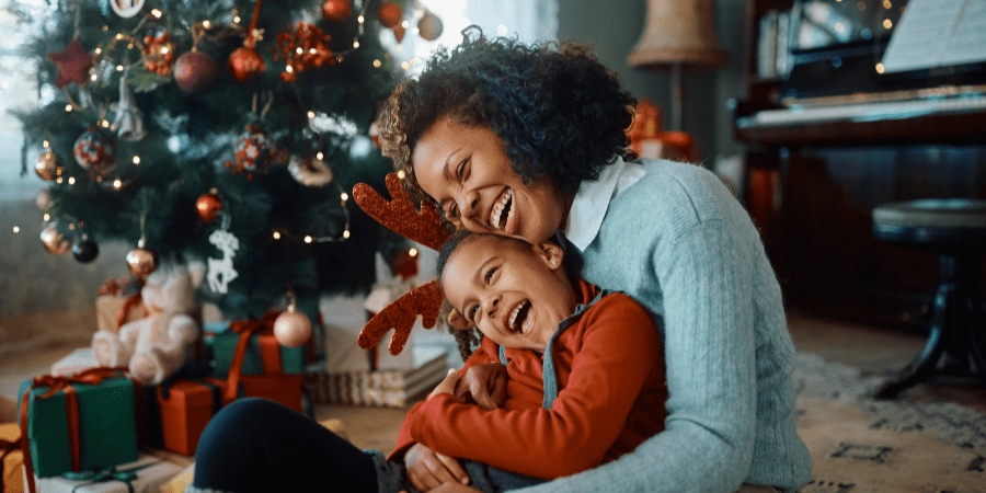 A mother embracing her young son in front of a Christmas tree.