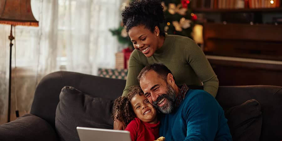 A family of three laughing on a couch with a christmas tree seen in the background.
