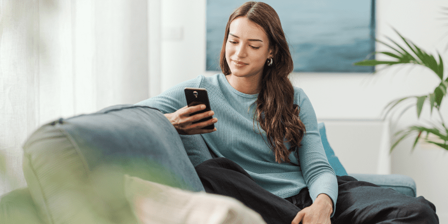 A young woman sitting on a couch using a smart phone.