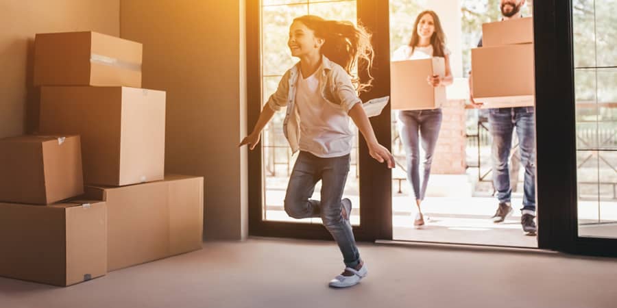 A happy family walking into a new home with the parents carrying boxes.