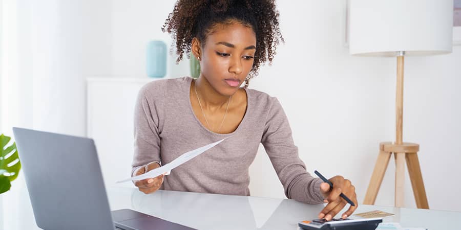 A young female sitting at a table using a calculator while holding a document.