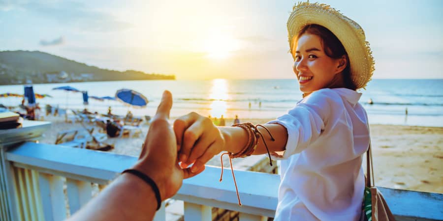 A young woman standing on a balcony looking over the shoreline during a beautiful sunset.