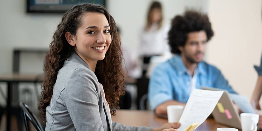 A young student sitting at a table holding papers and smiling.
