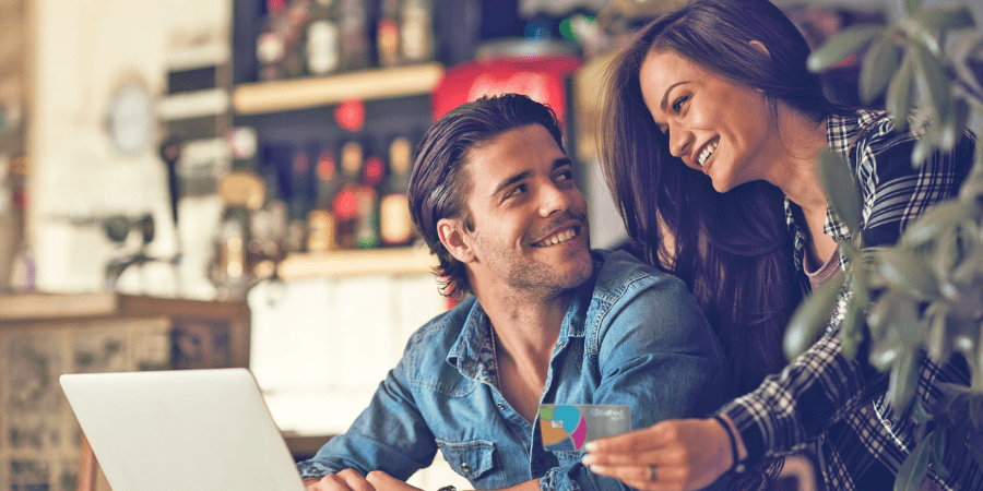 A man sits in front of a laptop while looking at a woman holding the EdFed Rewards Visa Credit Card.
