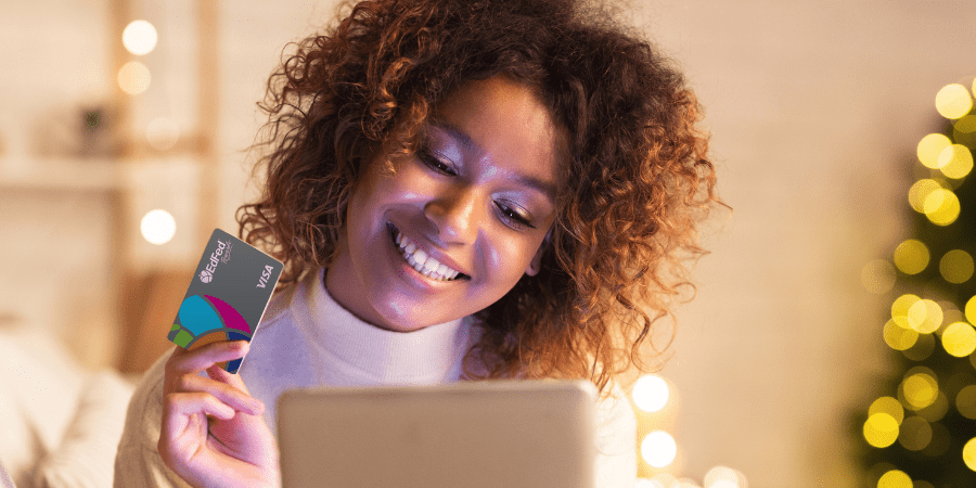 A woman smiling while holding the EdFed Visa credit card and looking at a laptop.