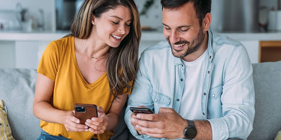 A young woman sitting next to a young man and both holding smart phones.