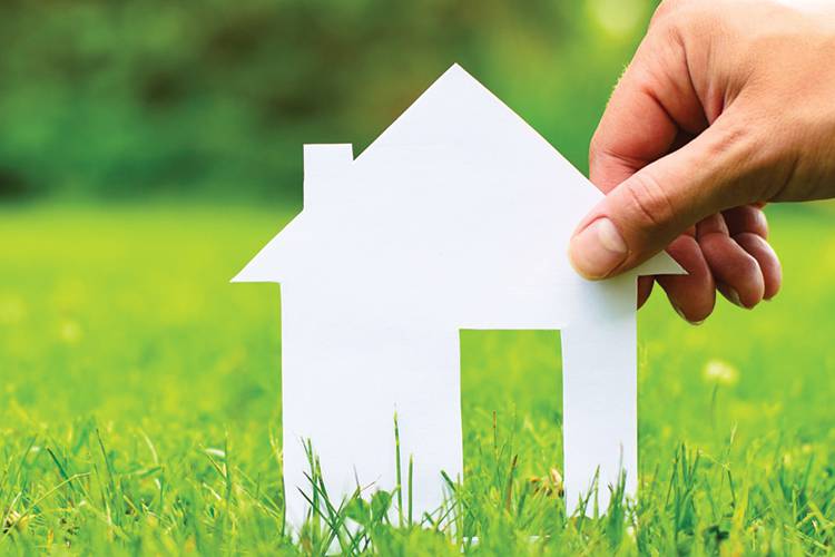 Hand holding up a white posterboard cutout of a house.