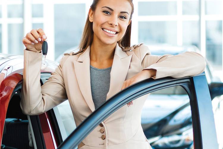 Smiling woman standing on drivers side of a red car holding a key.