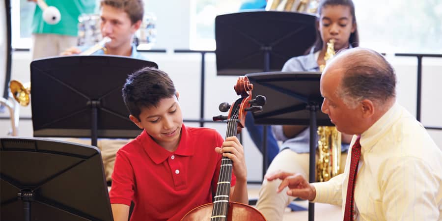 An elderly music teacher instructing a young student playing a cello.
