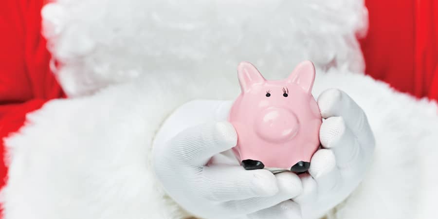 Santa Claus holding a small pink piggy bank.