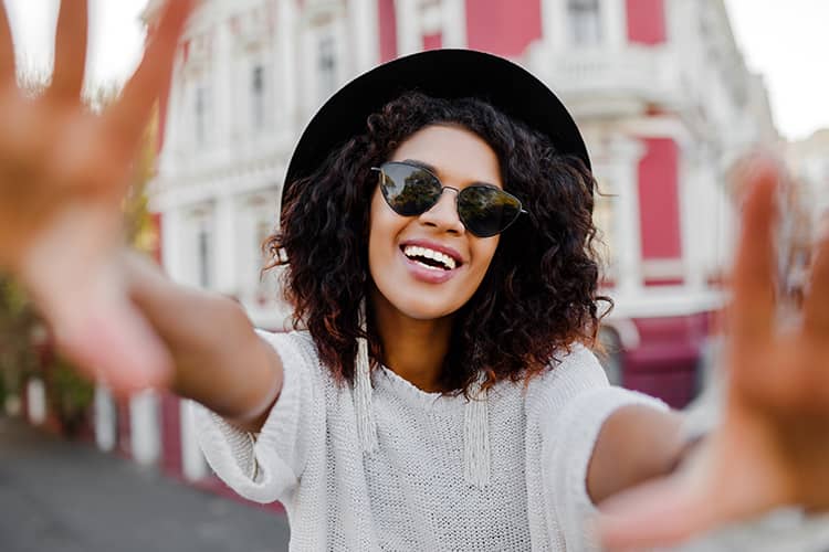 A young woman wearing sunglasses and a stylish hat smiling.