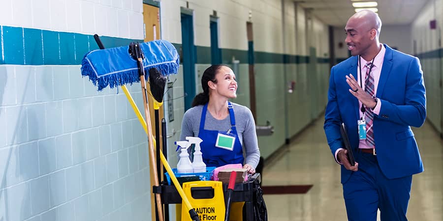 A school custodian and administrator conversing down a hallway.