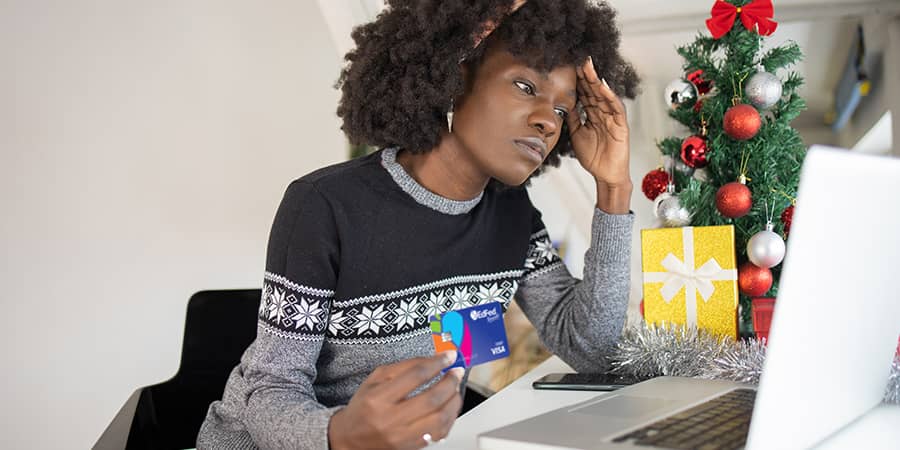 A woman in distress sitting at a desk in front of a laptop holding a credit card.