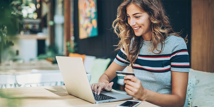 A young woman sitting at a table using a laptop while holding a credit card.