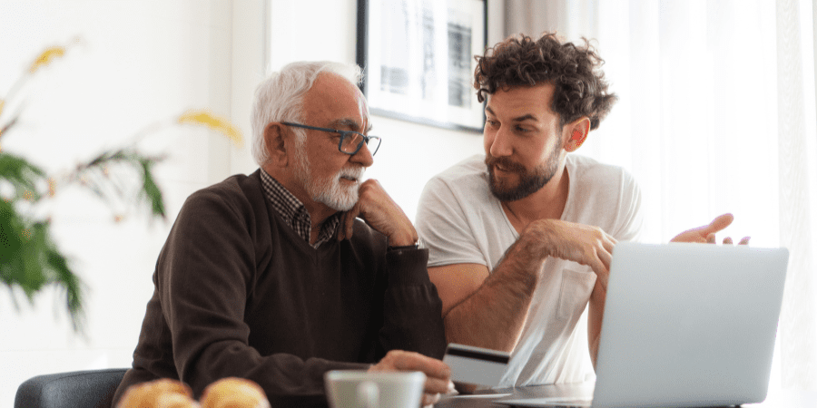 A middle-aged and eldery man sitting together looking at a laptop.