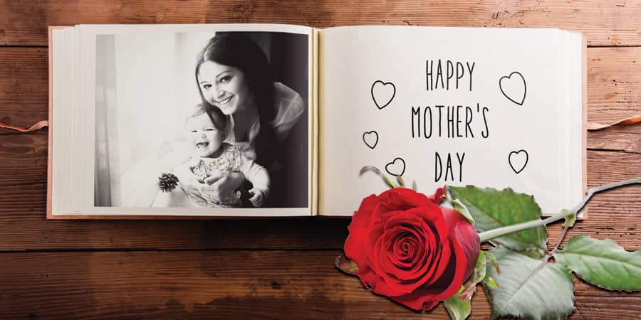 An open scrapbook laying on a wooden table and with roses over it showing a picture of a mom with an infant.