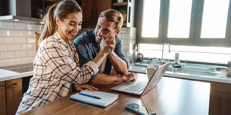 A couple sitting at a kitchen counter giving each other a high five.