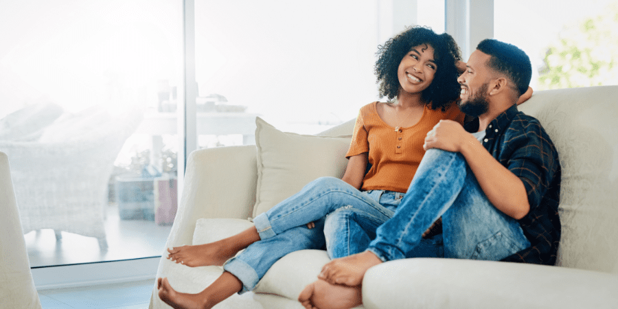 A young couple sitting on a couch smiling.